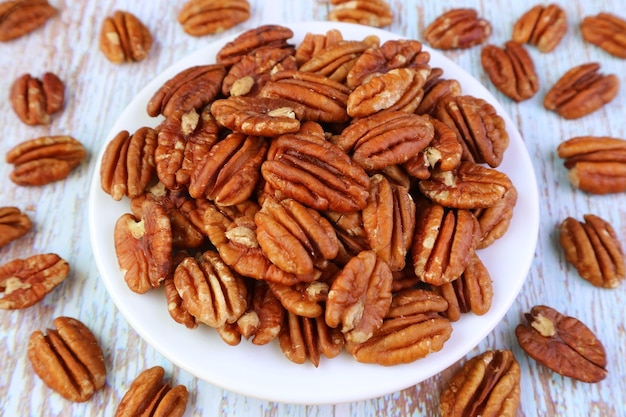 Plate of Dried Pecan Nuts with Some Kernels Scattered on Wooden Background