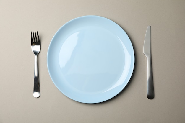 Plate, fork and knife on grey paper, top view