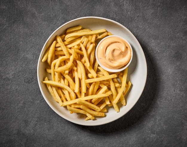 plate of french fries and mayonnaise dip on dark table top view