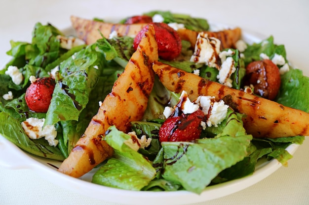 Plate of green salad with roasted pears, fresh strawberries and feta cheese