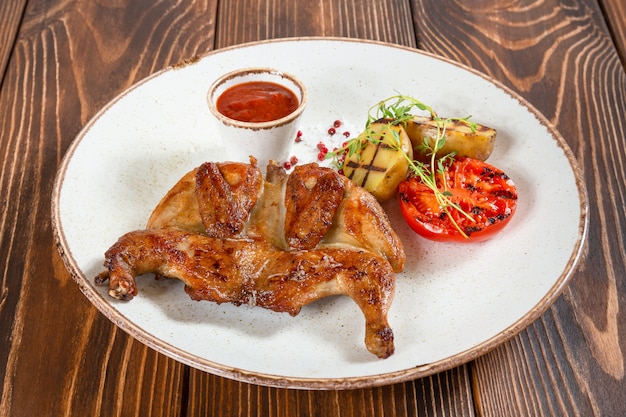 Plate of grilled chicken and vegetables with tomato sauce on wooden table