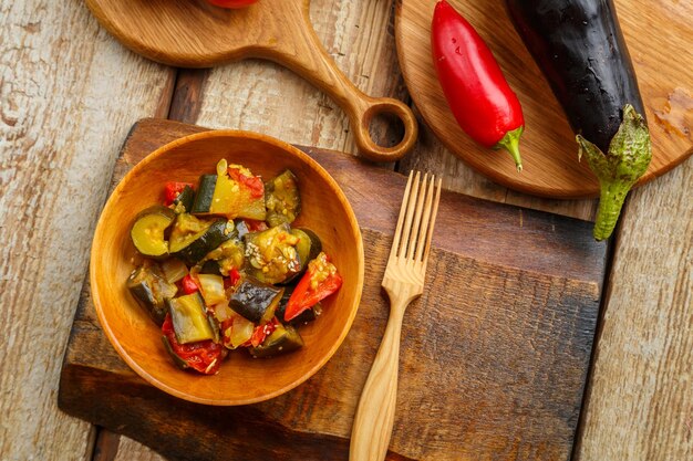 A plate of grilled vegetables next to tomatoes and eggplant on wooden boards next to a wooden fork