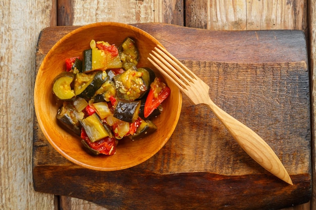 A plate of grilled vegetables on a wooden board next to a wooden fork