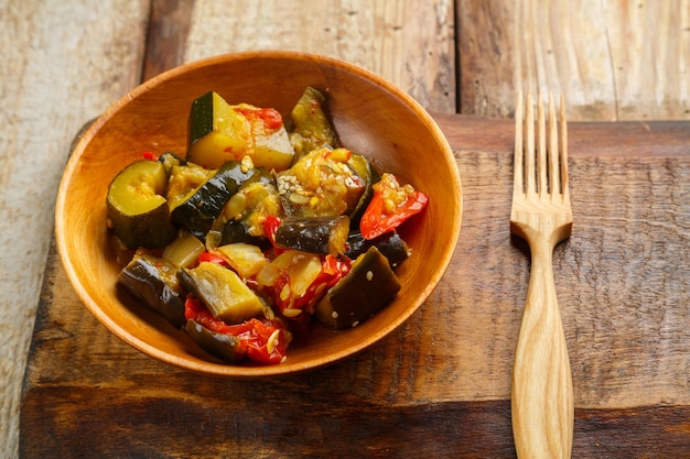 A plate of grilled vegetables on a wooden table on a wooden board next to a fork