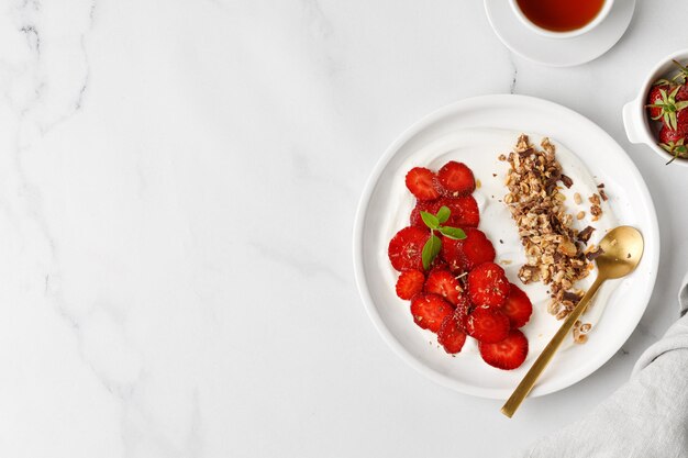 Plate of healthy yogurt with strawberry and granola on marble background Dessert with Strawberry