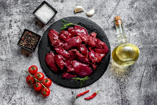 A plate of heart - shaped livers with olive oil and tomatoes on a gray background.