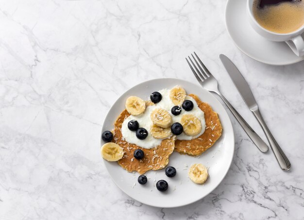 Plate of homemade breakfast with forest fruits and cup of coffee at marble table.