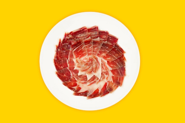 Plate of Iberian ham on yellow background, top view