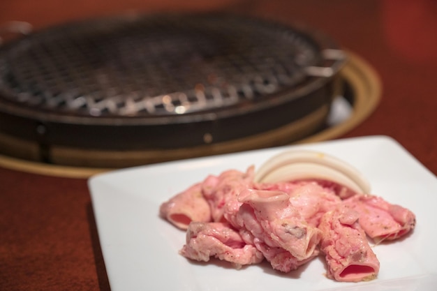 A plate of meat is on a table with a grill in the background.