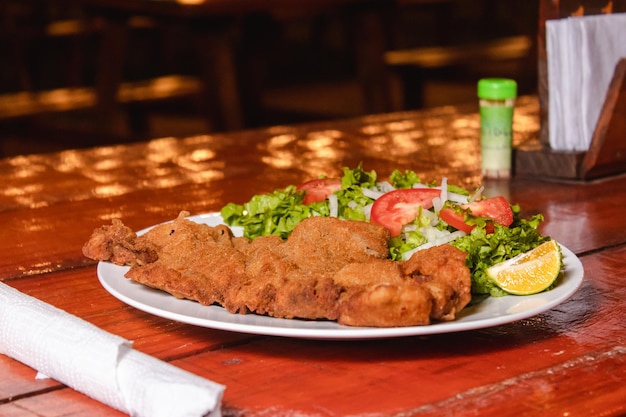 A plate of milanesa with salad on a wooden table