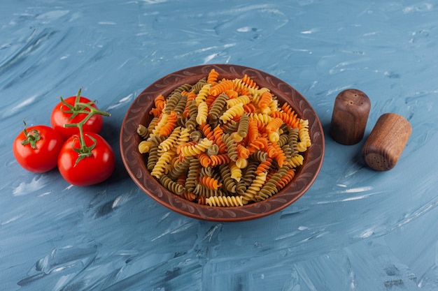 A plate of multi colored raw spiral pasta with fresh red tomatoes and spices.