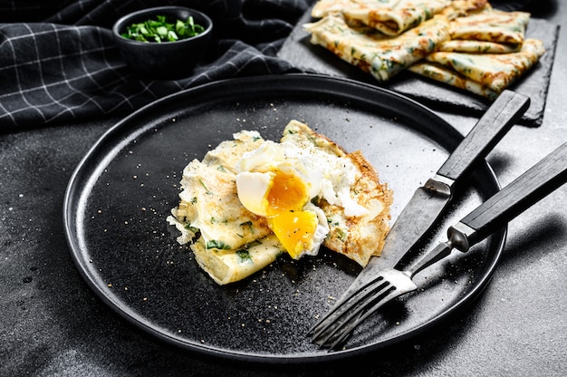 Plate of pancake stuffed with spinach and eggs. Black background.