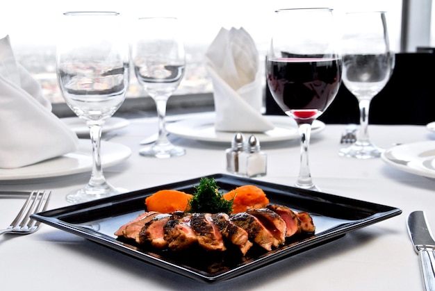 plate of pork loin and glass of red wine, restaurant table with white linen, food, gastronomy