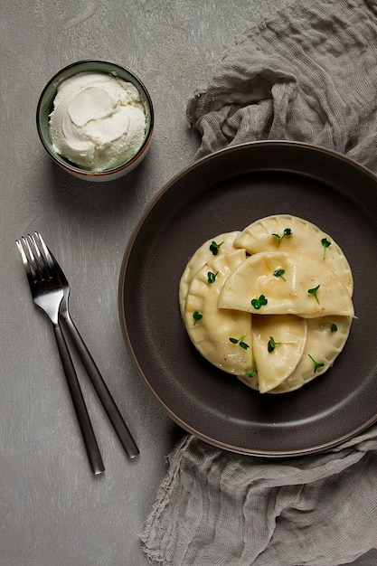 A plate of ravioli with a bowl of sour cream on the side.