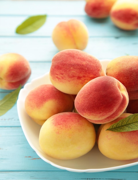 Plate of ripe peaches on blue background Vertical photo