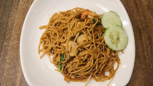 A plate of seafood fried noodles Indonesian style cuisine with some slice of cucumber Top View flat lay