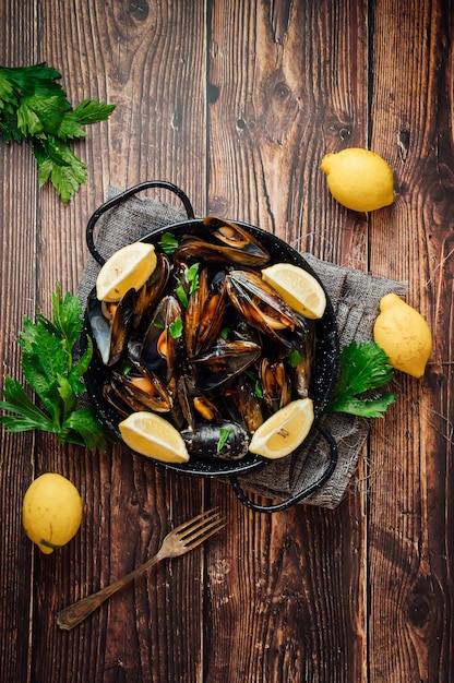 Plate of steamed mussels with lemon and parsley on a rustic wooden table.