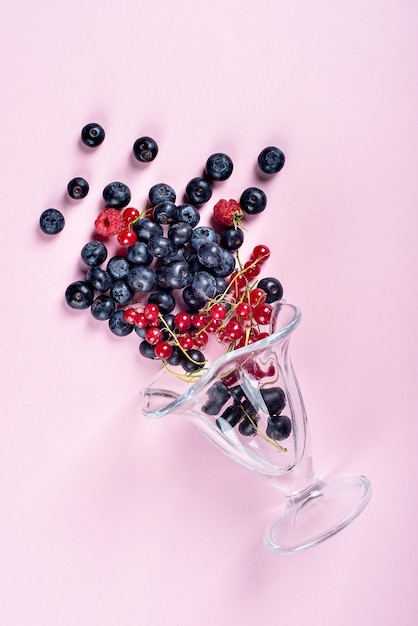 A plate of summer fruits on a pink background glasses from which berries are scattered