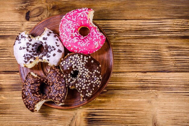 Plate with bitten glazed donuts on a wooden table Top view