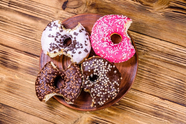 Plate with bitten glazed donuts on a wooden table Top view