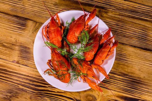 Plate with boiled crayfishes on wooden table Top view