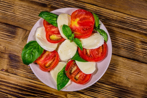 Plate with caprese salad italian salad with cherry tomatoes mozzarella cheese and basil leaves on wooden table Top view