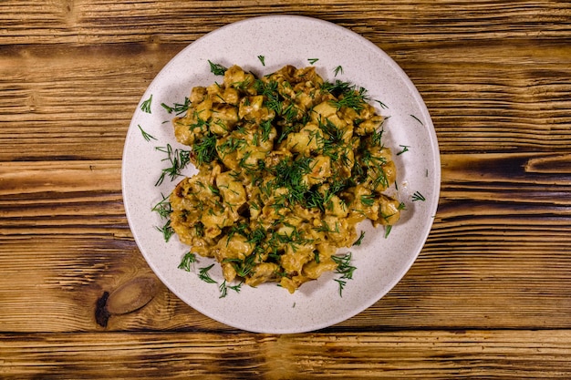 Plate with champignons stewed in sour cream on a wooden table. Top view