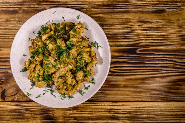 Photo plate with champignons stewed in sour cream on a wooden table top view