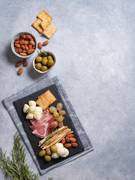 A plate with cheese ham mozzarella olives nuts grapes and other snacks on a black stone board Antipasto The concept of Italian food Top view and copy space