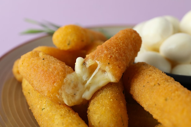 Plate with cheese sticks, mozzarella and rosemary on violet background