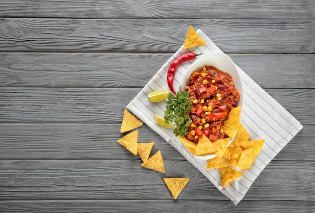 Plate with chili con carne and nacho chips on wooden background