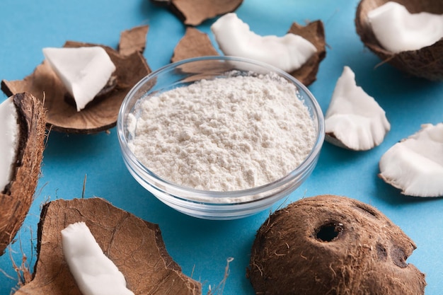 Photo plate with coconut gluten free flour and nuts on blue background, closeup. organic ingredients for cooking vegan meals. nutritious exotic nuts.