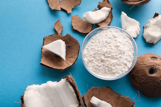 Plate with coconut gluten free flour and nuts on blue background, top view, copy space. Organic ingredients for cooking vegan meals. Nutritious exotic nuts.