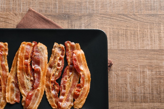 Plate with cooked bacon rashers on table