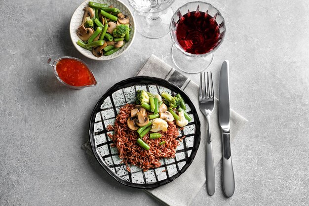 Plate with delicious brown rice and vegetables on table