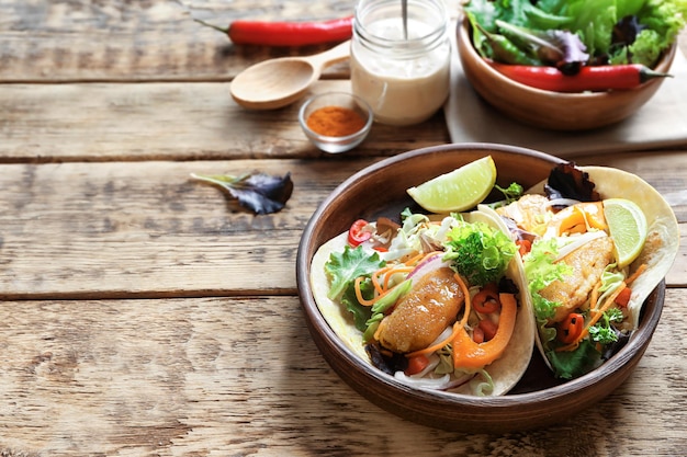 Plate with delicious fish tacos on wooden table