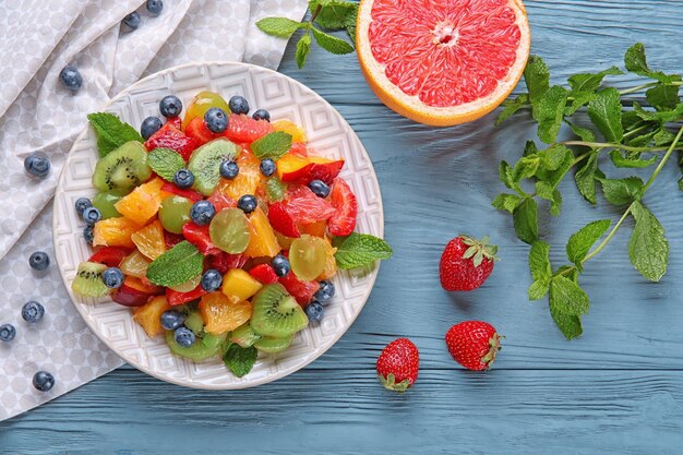 Photo plate with delicious fruit salad on wooden table