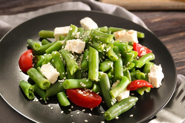 Plate with delicious green beans salad on wooden table closeup