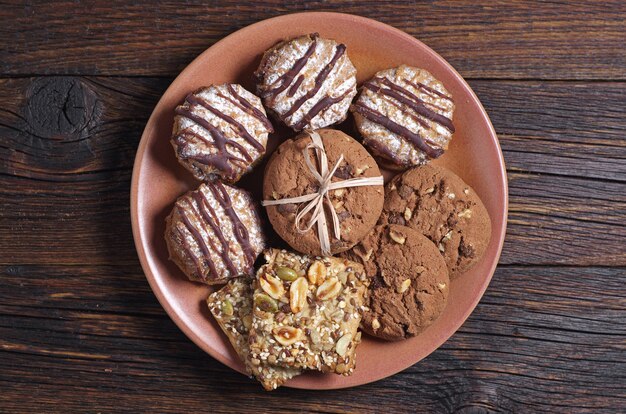 Plate with different cookies on dark wooden table, top view