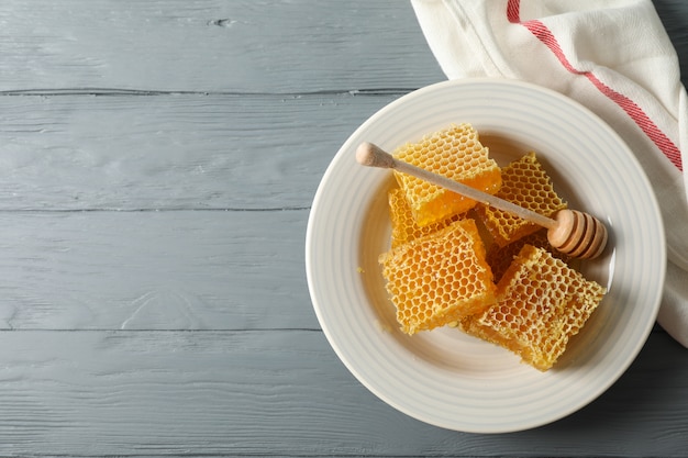 Plate with dipper and honeycombs on wooden background, space for text