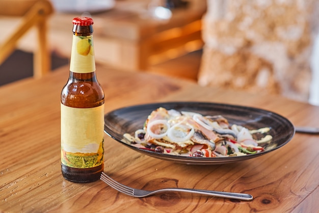 A plate with fish herring and a bottle of beer a wooden table