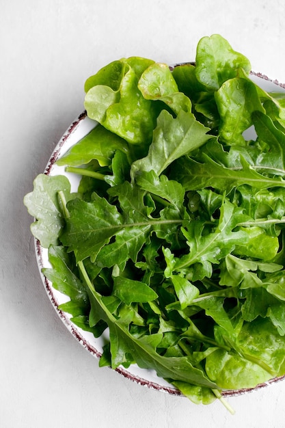 Plate with fresh arugula plants on white background Top view food Healthy vegetarian dish