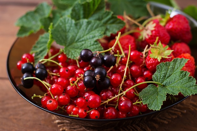 Plate with fresh berries (strawberries and currants) on dark wooden table