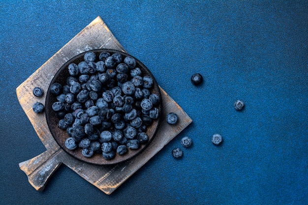 Plate with fresh blueberries on a blue background. Board with fresh berries. View from above. Focus on the plate