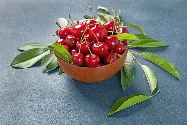 Plate with fresh cherries with green leaves. Black background.