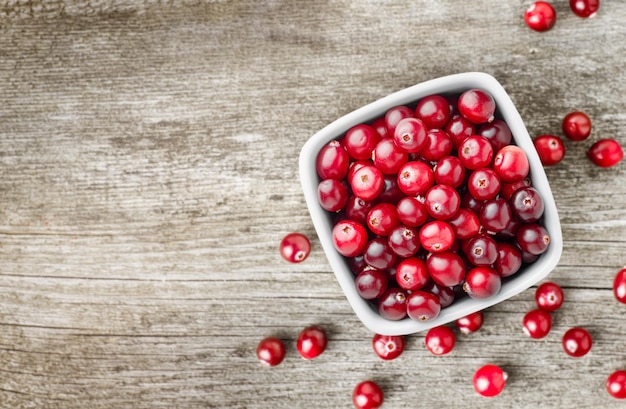 Plate with fresh cranberries on wooden background, top view