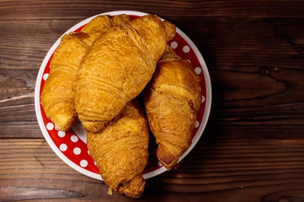 Plate with fresh croissants on wooden table. Top view