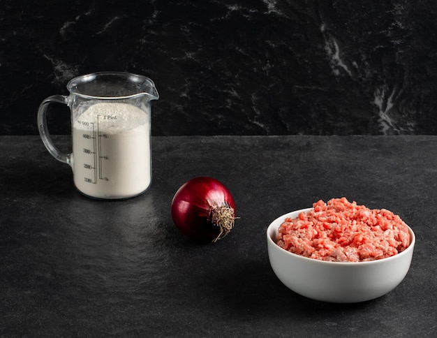 Plate with fresh ground beef red onion measuring cup with flour on a grey black background space for textxA