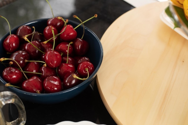 Photo plate with fresh organic cherries on kitchen table near wooden chopping board closeup