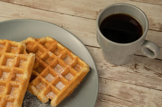 Plate with freshly baked waffles with a cup of black coffee on a light wooden background breakfast snack pastry concept